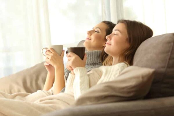 two women sitting on couch relaxed and comfortable with a cup of coffee in their hands, happy thanks to boerne heater repair